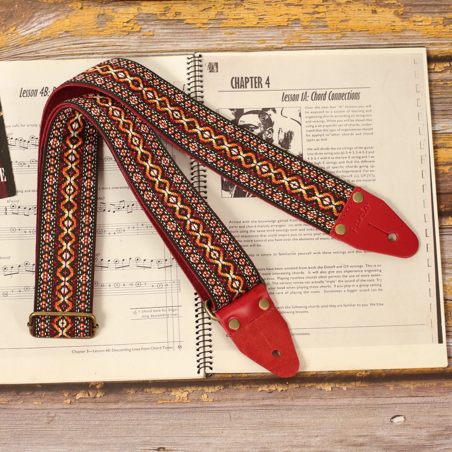 Full view of the Red Marley vintage red and orange jacquard guitar strap displayed on a sheet music book, highlighting its handcrafted woven pattern and classic reggae-inspired design.