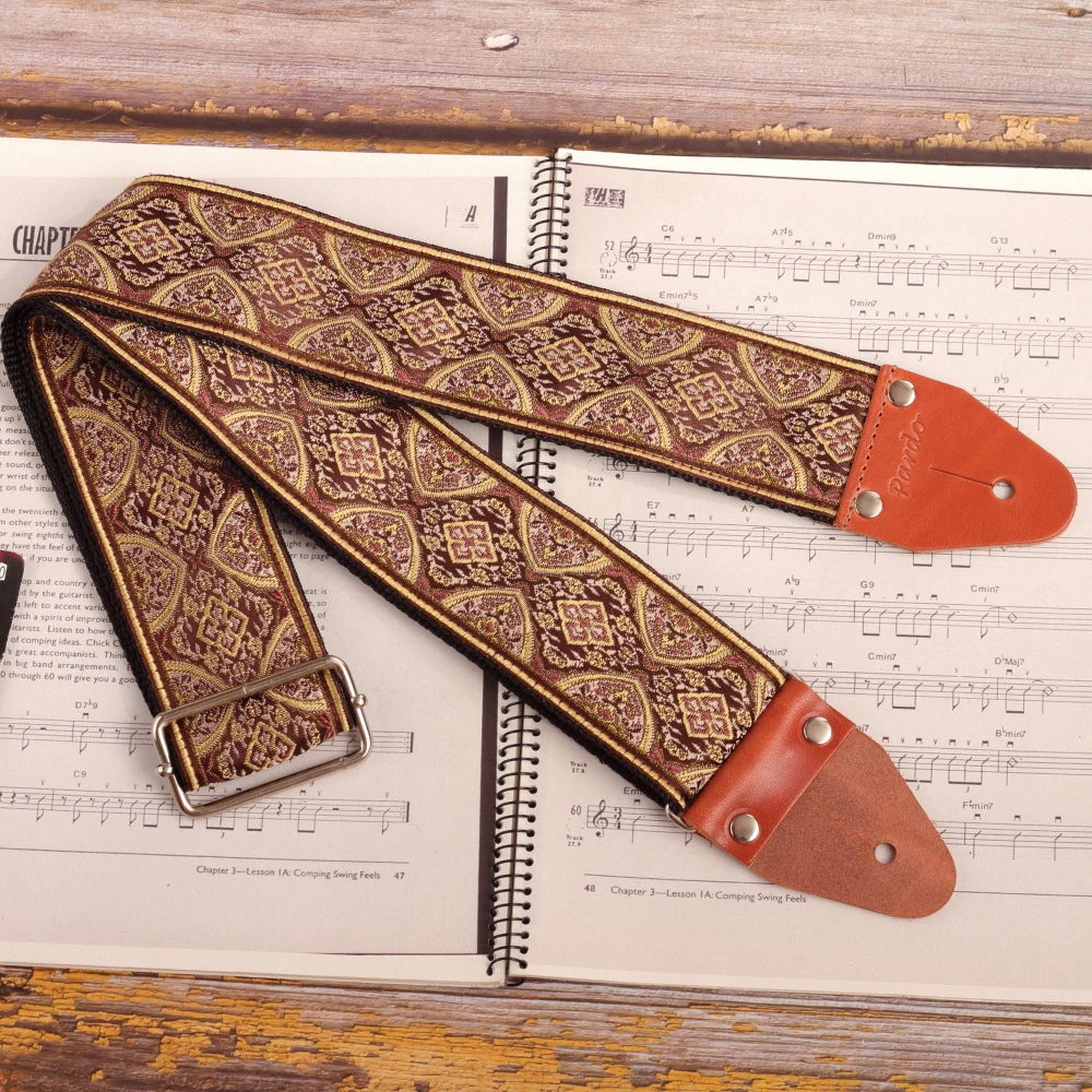wide long psychedelic jacquard guitar strap in brown tones placed on sheet music